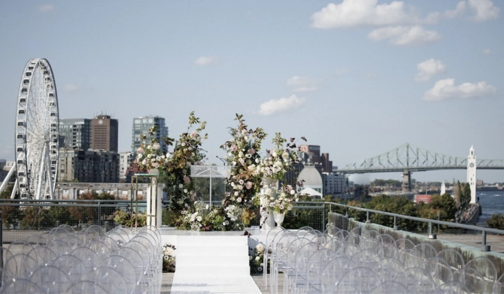 “Outdoor rooftop wedding ceremony at Le Belvédère du Vieux-Port in Montreal — floral arch with panoramic views of the St. Lawrence River, Ferris wheel, and Jacques Cartier Bridge, ideal for unique destination weddings in Canada.
