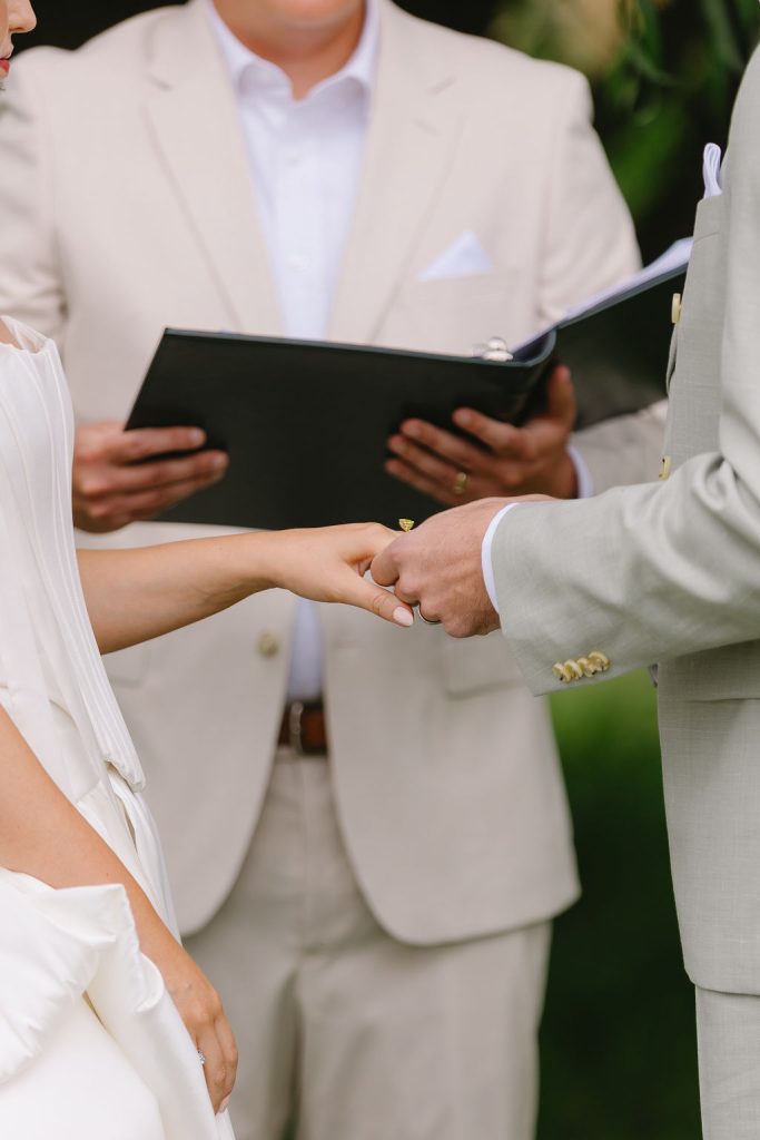 Close-up of couple exchanging wedding rings during outdoor ceremony in Canada, officiant holding marriage documents — symbolic image representing legal requirements for getting married in Canada.