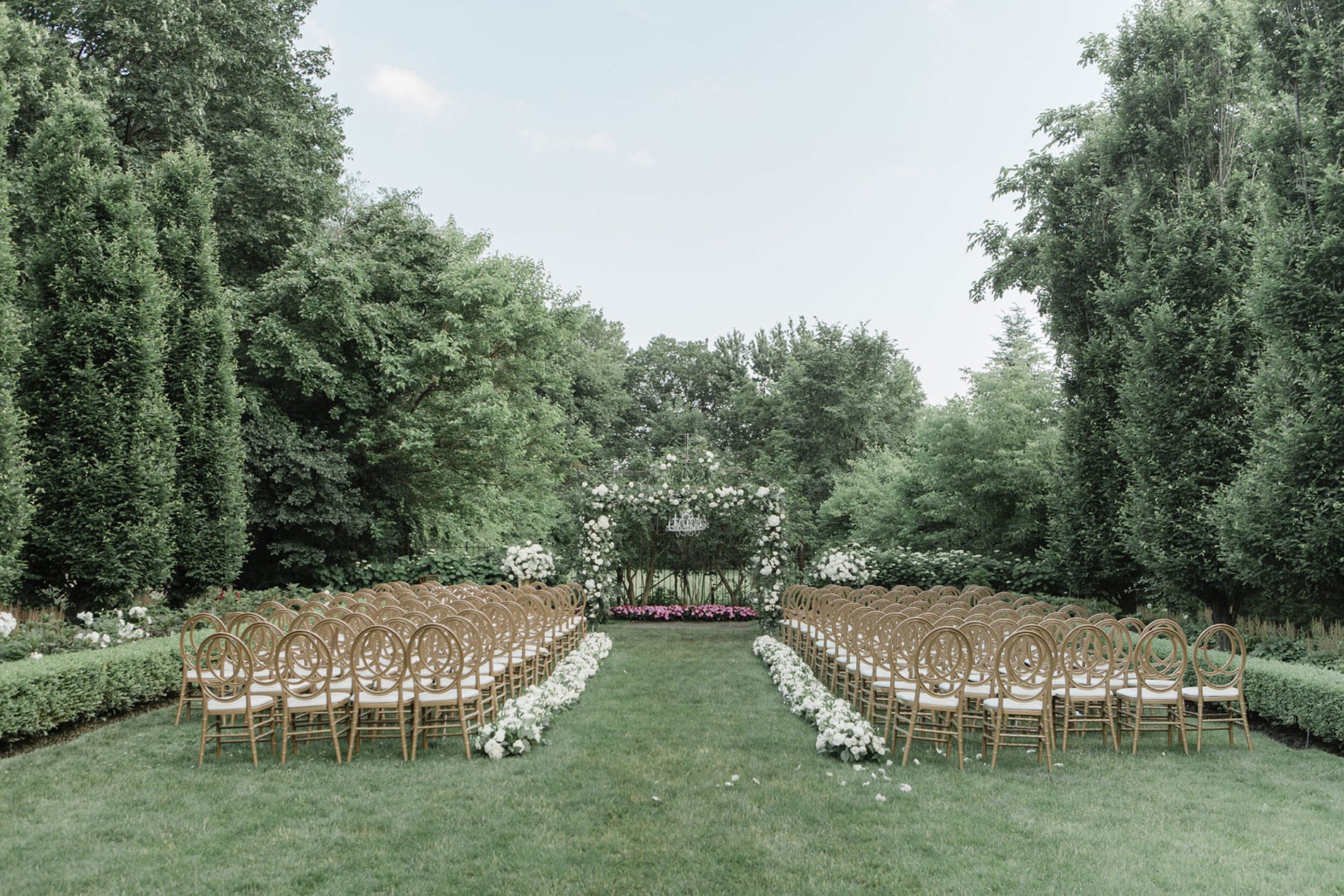 Outdoor garden wedding ceremony setup at a luxury Toronto wedding venue featuring gold chameleon chairs and white floral aisle markers.