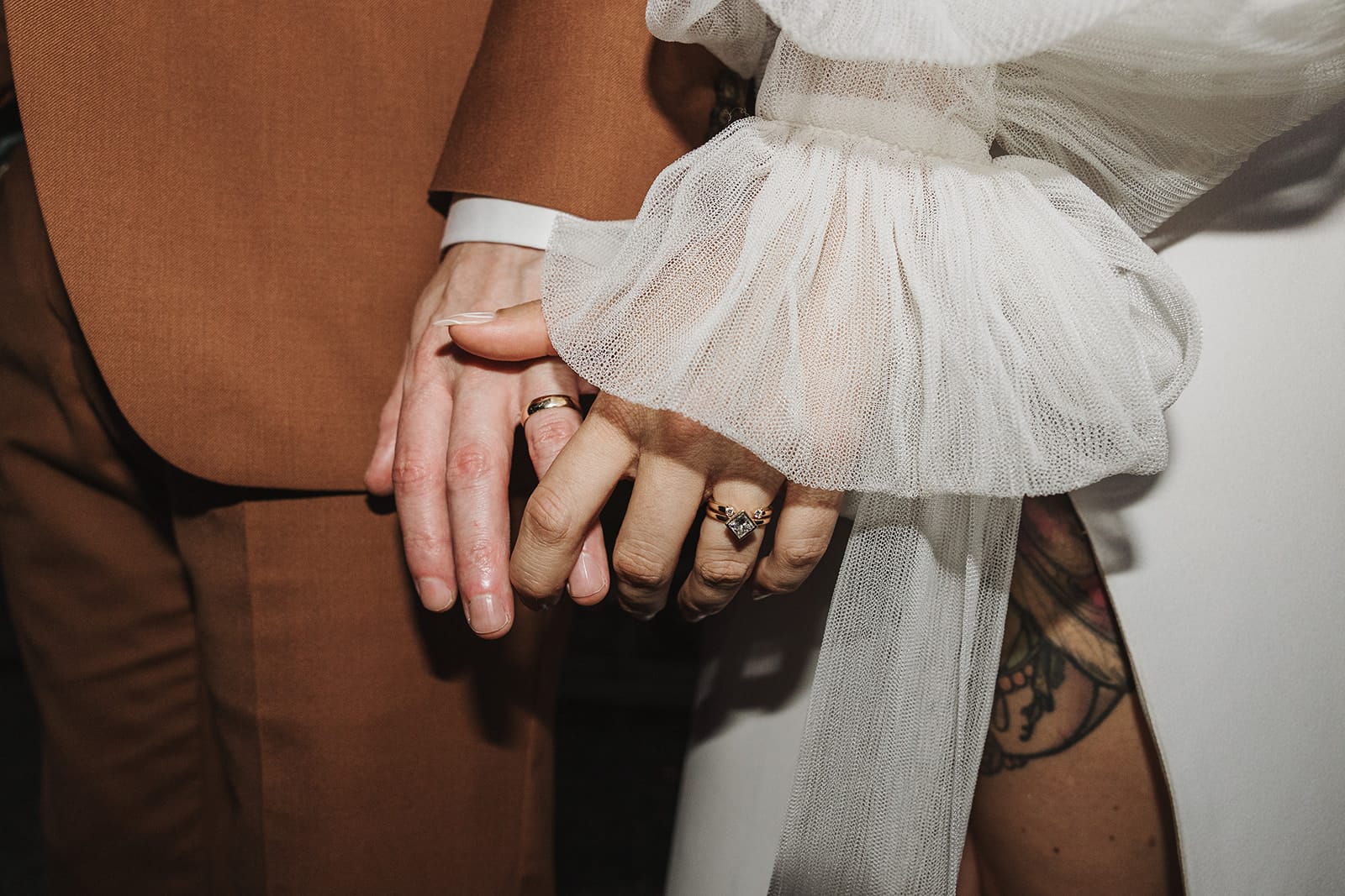 Detailed close-up of a bride and groom holding hands, showcasing the wedding ring and dress details—Thistle & Thorne.