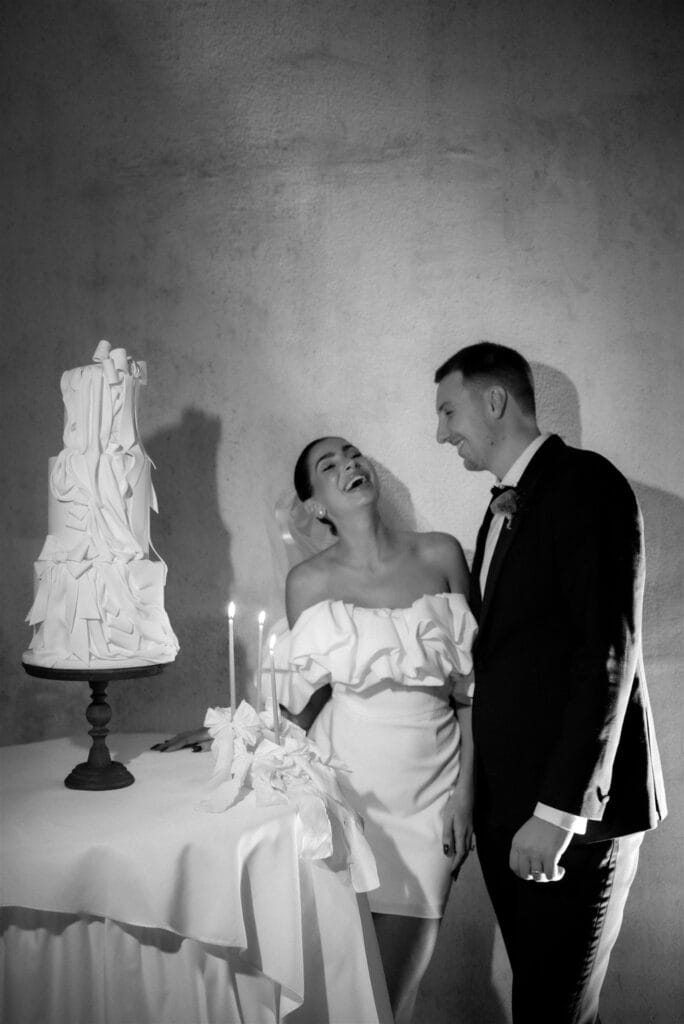 Intimate moment of a laughing bride and groom cutting a modern tiered wedding cake, illustrating boutique styled shoot elegance - Thistle & Thorne