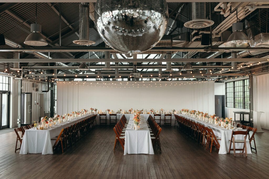 Spacious industrial loft wedding venue set up for a large reception with parallel banquet tables, showcasing Montreal wedding cost considerations - Thistle & Thorne