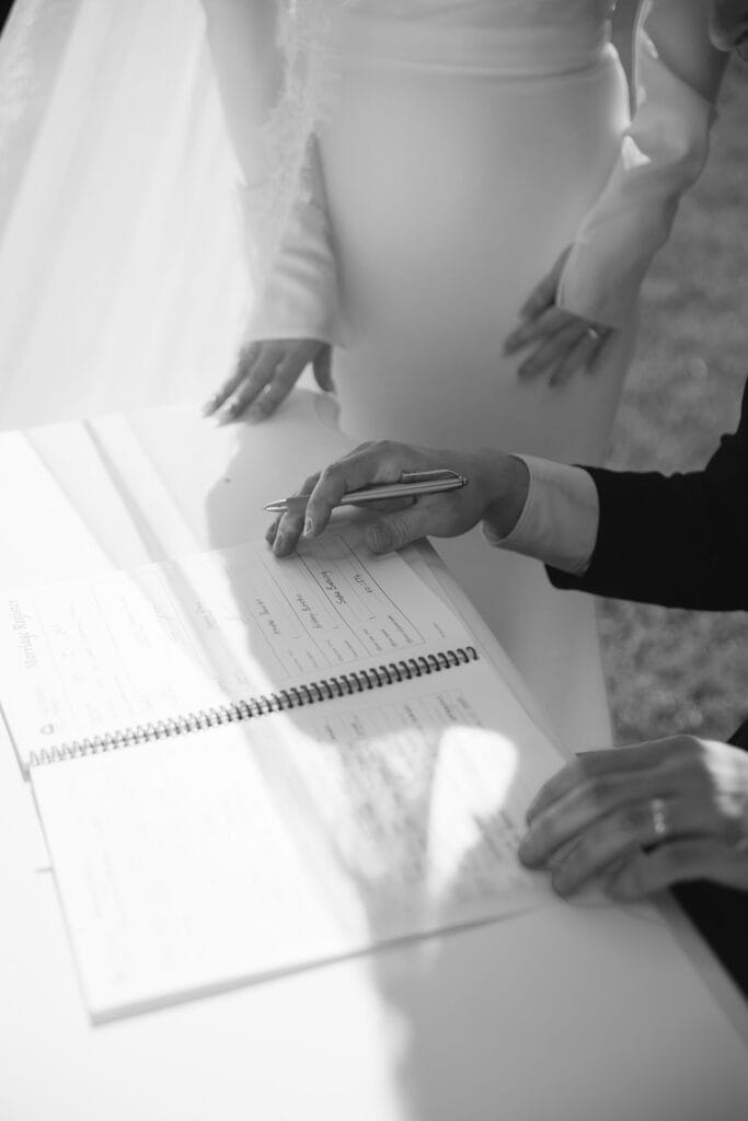 Close-up of a couple signing the official marriage register book during an elegant wedding ceremony - Thistle & Thorne