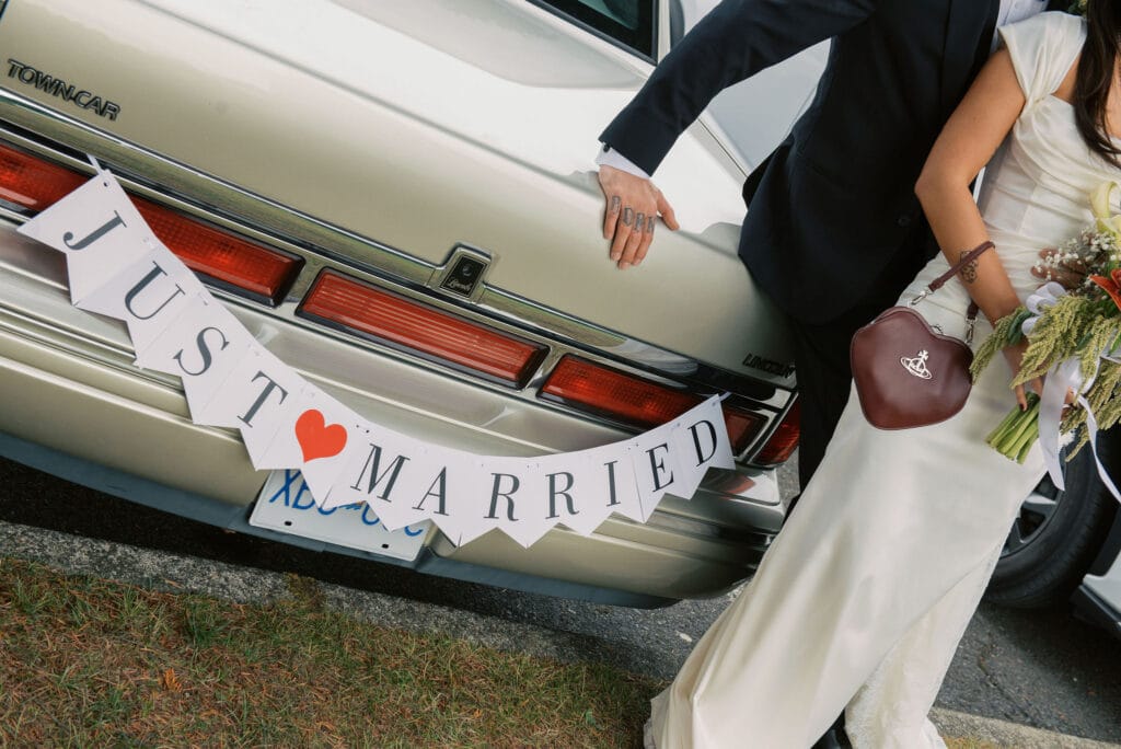 Bride and groom standing next to a vintage Lincoln getaway car with a Just Married banner - Thistle & Thorne