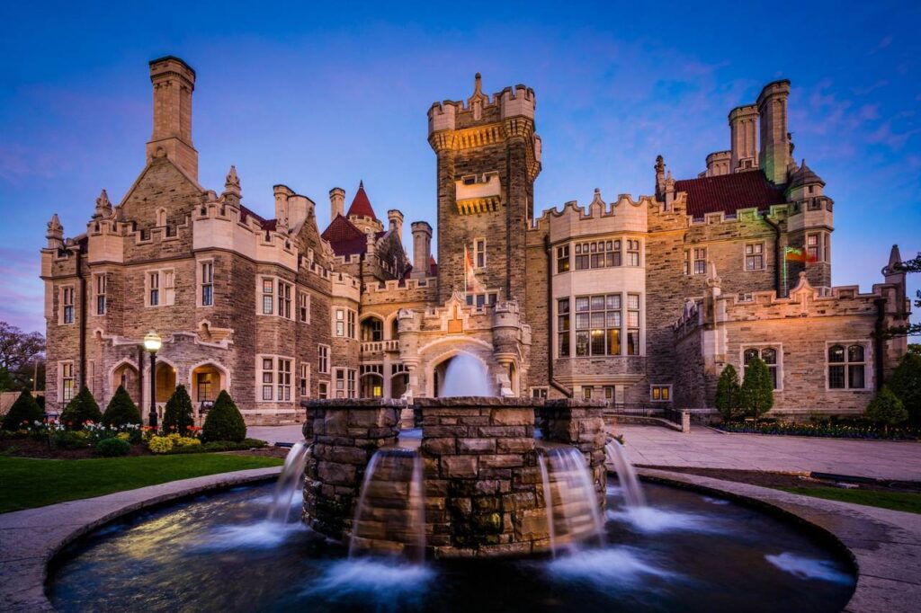 casa loma castle in toronto lit up at dusk with a large stone water fountain in the foreground, serving as a historic luxury wedding venue.