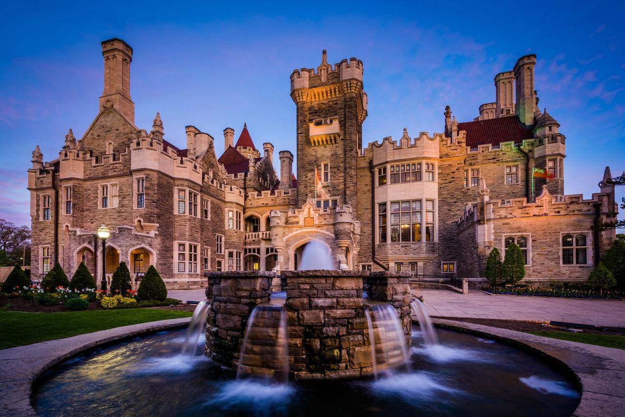 casa loma castle in toronto lit up at dusk with a large stone water fountain in the foreground, serving as a historic luxury wedding venue.